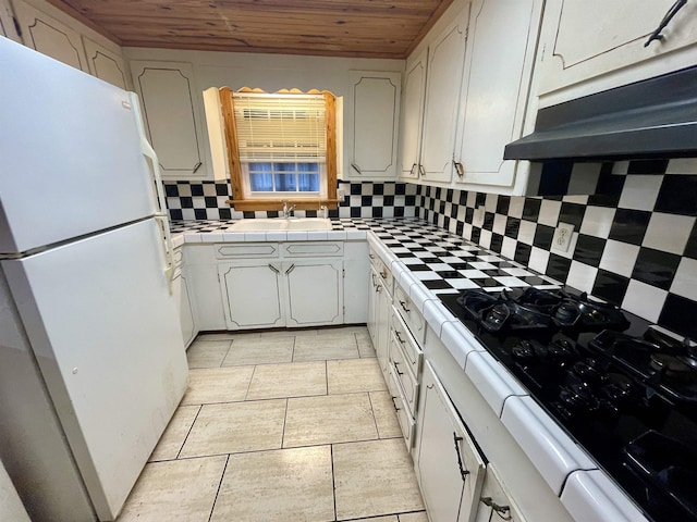 kitchen with white fridge, sink, white cabinetry, wooden ceiling, and tile countertops