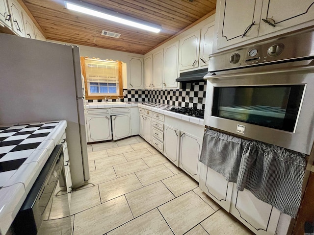 kitchen with double oven, white refrigerator, tile countertops, wood ceiling, and decorative backsplash