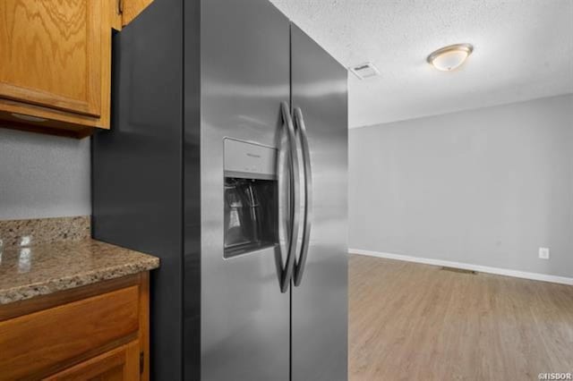 kitchen with light hardwood / wood-style flooring, stainless steel fridge, light stone countertops, and a textured ceiling