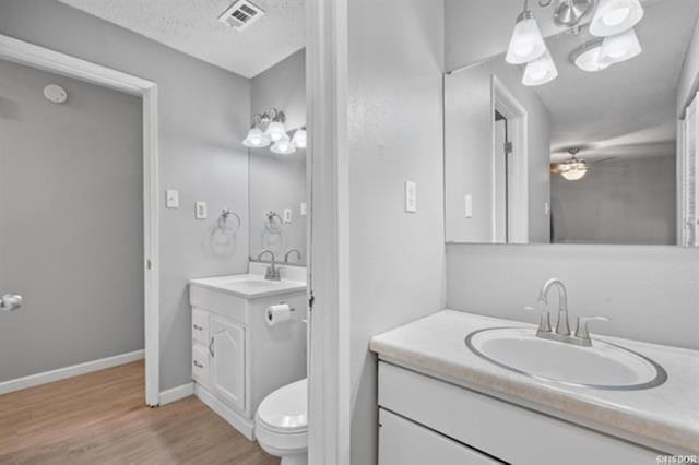 bathroom with ceiling fan, vanity, wood-type flooring, a textured ceiling, and toilet