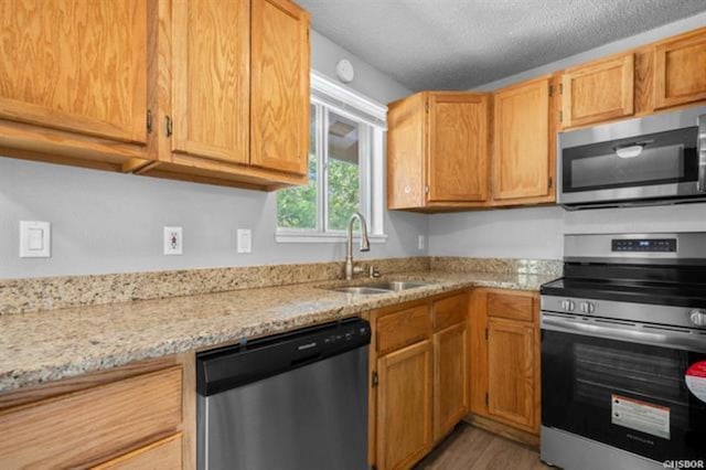 kitchen with sink, a textured ceiling, appliances with stainless steel finishes, dark hardwood / wood-style flooring, and light stone countertops