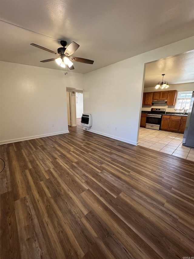 unfurnished living room with ceiling fan with notable chandelier, light wood-type flooring, and heating unit