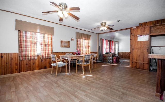 dining room featuring crown molding, ceiling fan, wood-type flooring, and wood walls