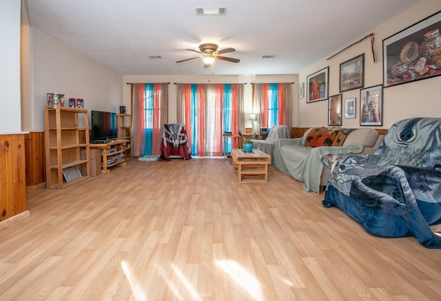 living room with ceiling fan, wooden walls, and light hardwood / wood-style floors