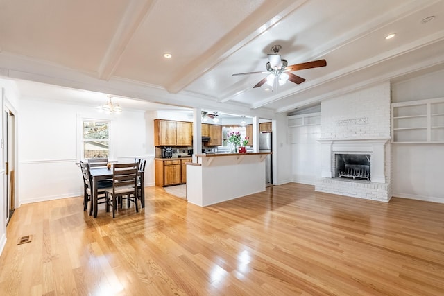 kitchen featuring ceiling fan with notable chandelier, a fireplace, stainless steel refrigerator, kitchen peninsula, and light hardwood / wood-style flooring