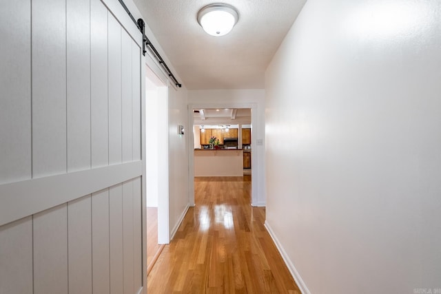 hall featuring a barn door, a textured ceiling, and light wood-type flooring