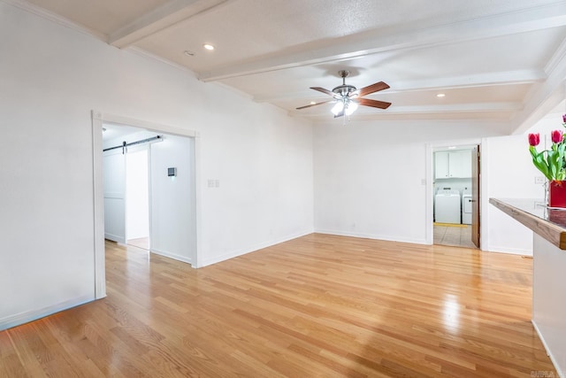 unfurnished room with ceiling fan, a barn door, light wood-type flooring, and washer and clothes dryer