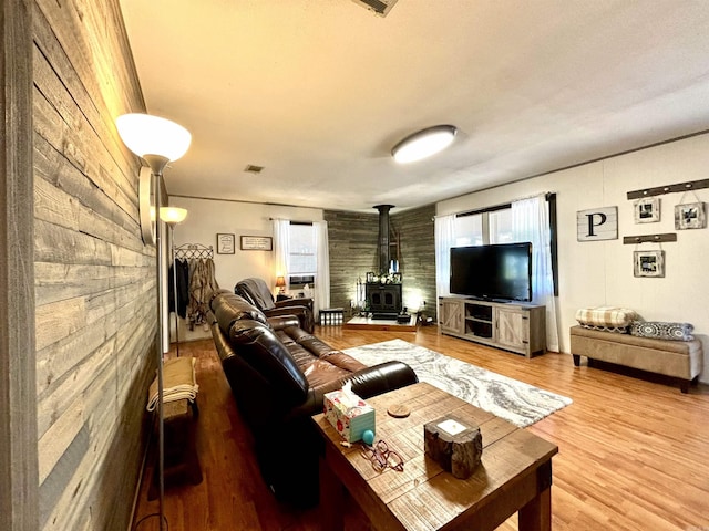 living room with hardwood / wood-style flooring, wood walls, and a wood stove