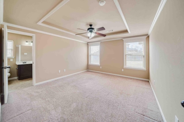 unfurnished bedroom with ensuite bath, ceiling fan, ornamental molding, light colored carpet, and a raised ceiling