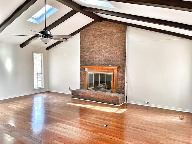 unfurnished living room with a brick fireplace, wood-type flooring, vaulted ceiling with skylight, and ceiling fan