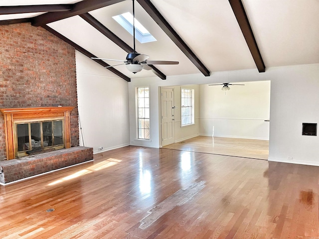 unfurnished living room with a brick fireplace, a skylight, light hardwood / wood-style floors, and beamed ceiling