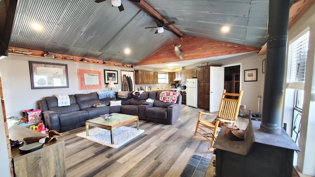 living room with lofted ceiling with beams, a wood stove, ceiling fan, a wall unit AC, and light hardwood / wood-style flooring