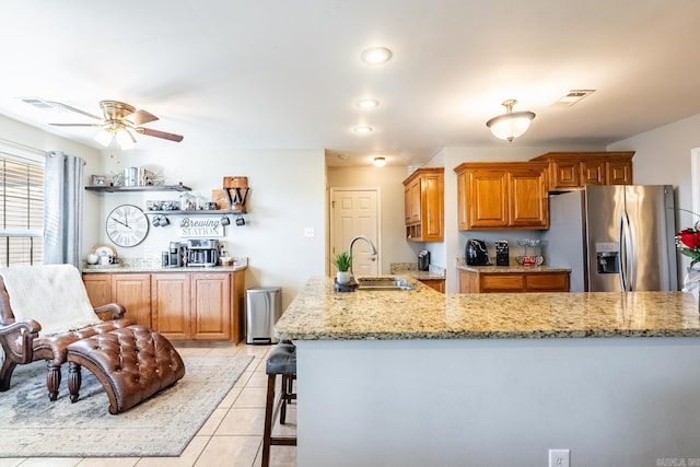 kitchen featuring light tile patterned floors, a breakfast bar, sink, stainless steel fridge, and light stone countertops