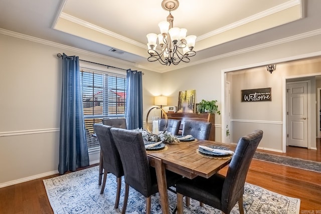 dining area featuring a raised ceiling, crown molding, dark wood-type flooring, and a notable chandelier