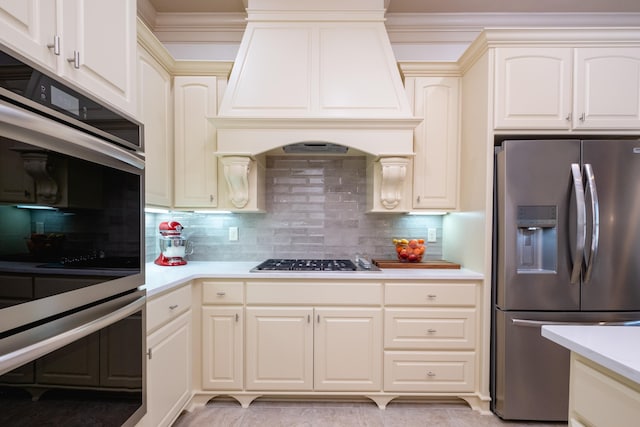 kitchen featuring cream cabinets, appliances with stainless steel finishes, tasteful backsplash, and custom range hood