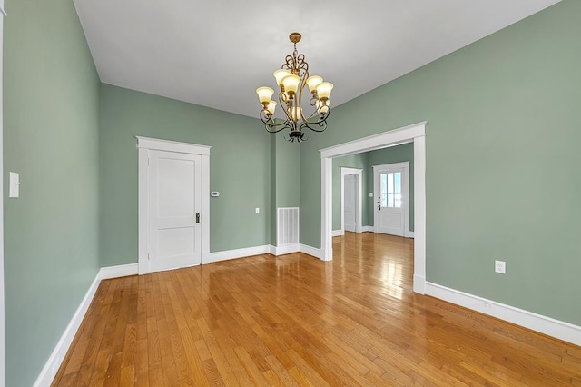 spare room with light wood-type flooring and a notable chandelier