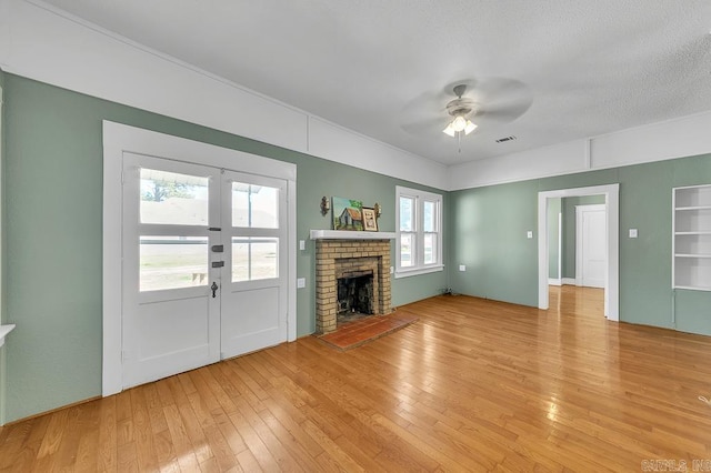 unfurnished living room featuring french doors, a textured ceiling, ceiling fan, light hardwood / wood-style floors, and a brick fireplace