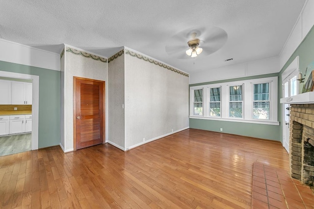 unfurnished living room featuring a fireplace, a textured ceiling, ceiling fan, and light hardwood / wood-style flooring