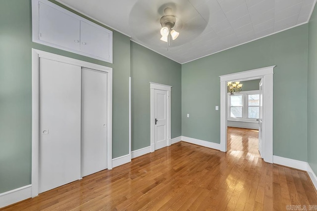 unfurnished bedroom with ceiling fan with notable chandelier, light wood-type flooring, and a closet