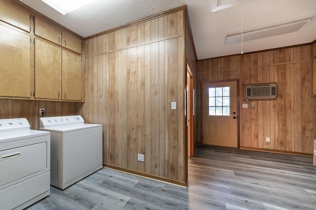 laundry area with independent washer and dryer, light hardwood / wood-style flooring, a textured ceiling, a wall mounted air conditioner, and cabinets