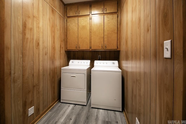 laundry area featuring light hardwood / wood-style flooring, independent washer and dryer, cabinets, and wooden walls