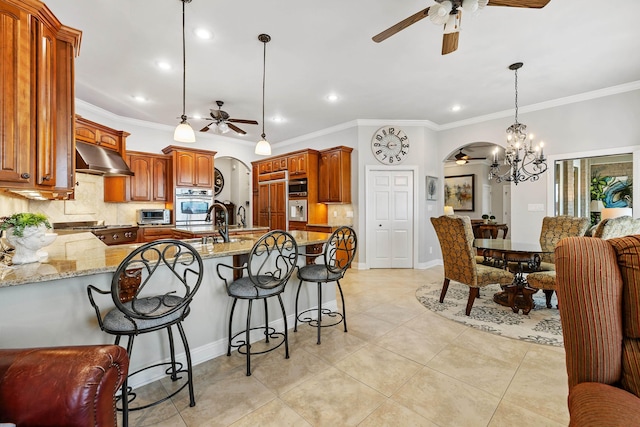 kitchen featuring built in appliances, tasteful backsplash, light stone counters, decorative light fixtures, and ceiling fan with notable chandelier