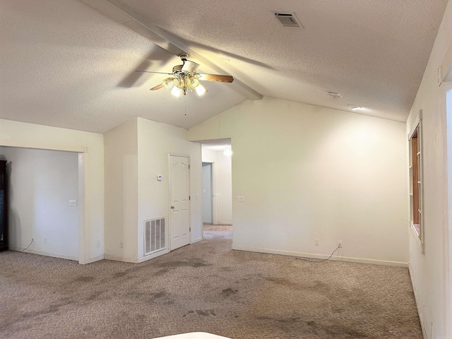 carpeted empty room featuring ceiling fan, vaulted ceiling with beams, and a textured ceiling