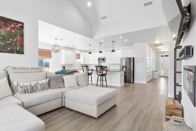 living room with high vaulted ceiling, light wood-type flooring, visible vents, and recessed lighting