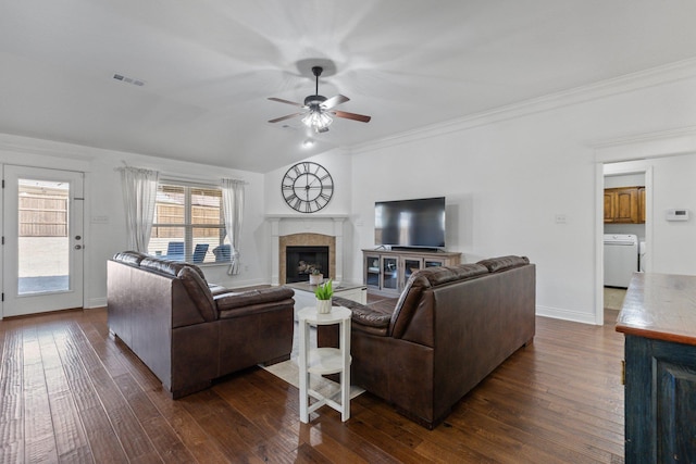 living room with a tile fireplace, vaulted ceiling, ceiling fan, dark wood-type flooring, and washer / dryer