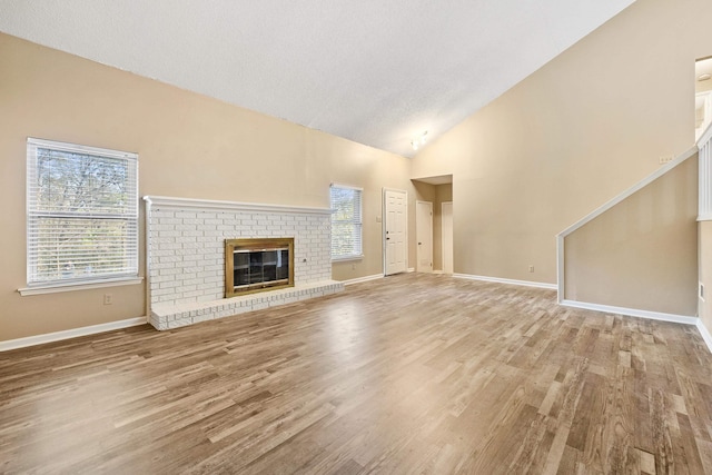 unfurnished living room featuring light hardwood / wood-style floors, high vaulted ceiling, a textured ceiling, and a fireplace