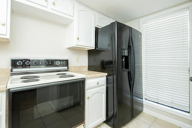 kitchen with white cabinets, light tile patterned floors, black fridge, and electric range