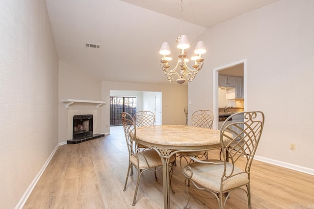 dining room featuring light wood-type flooring, a tiled fireplace, lofted ceiling, and a notable chandelier