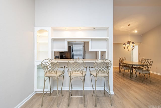 kitchen featuring hanging light fixtures, a kitchen breakfast bar, a notable chandelier, light wood-type flooring, and kitchen peninsula