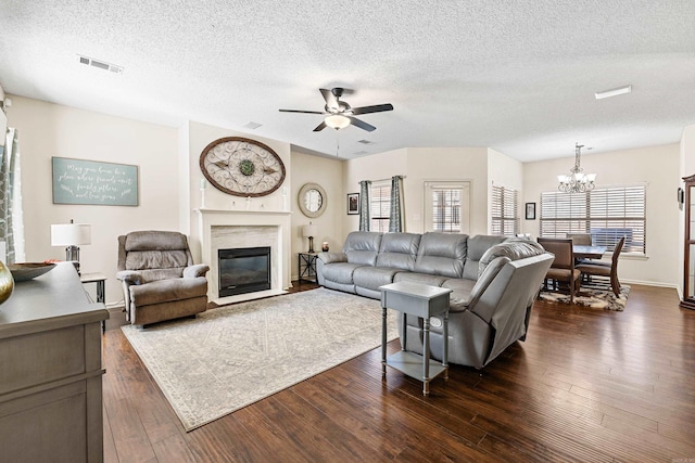 living room with ceiling fan with notable chandelier, dark wood-type flooring, a high end fireplace, and a textured ceiling