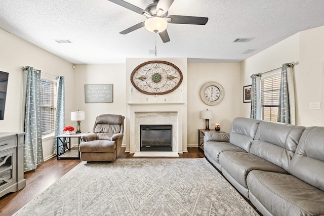 living room featuring a high end fireplace, ceiling fan, dark wood-type flooring, and a textured ceiling