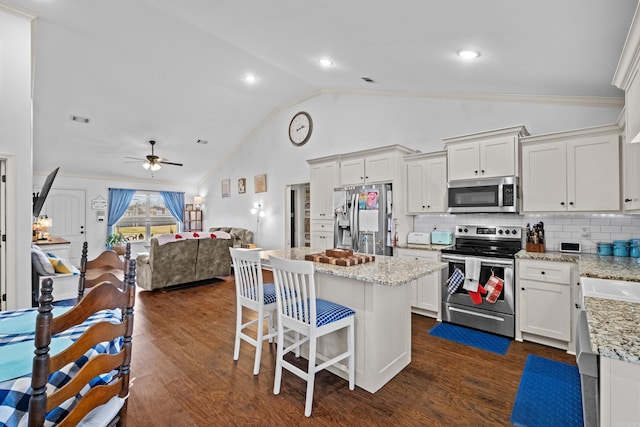 kitchen with appliances with stainless steel finishes, light stone counters, white cabinets, and lofted ceiling