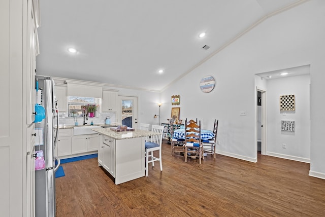 kitchen with vaulted ceiling, a kitchen island, white cabinets, and a breakfast bar