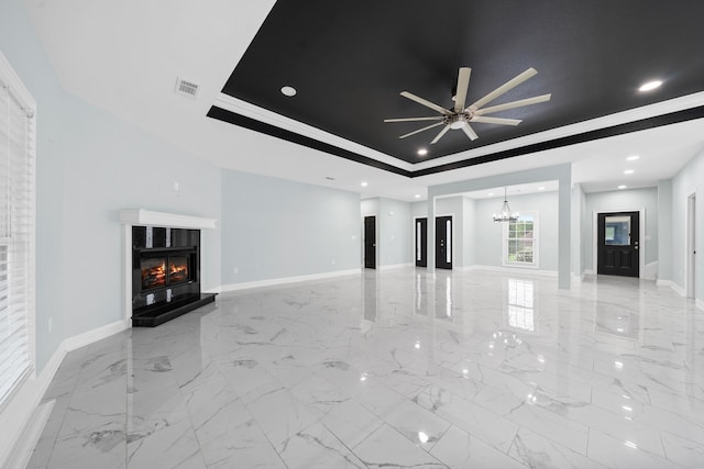 unfurnished living room with a tray ceiling, crown molding, and ceiling fan with notable chandelier