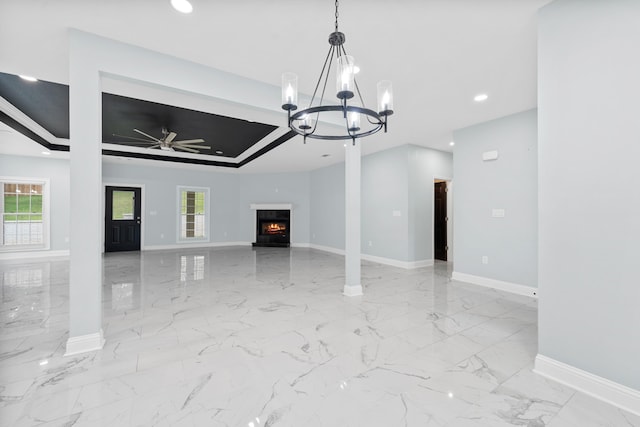 unfurnished living room with a raised ceiling, plenty of natural light, and ceiling fan with notable chandelier