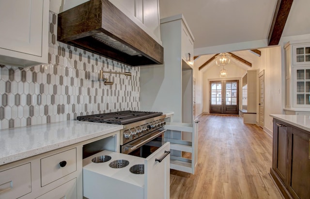 kitchen with double oven range, premium range hood, white cabinets, light stone countertops, and beam ceiling