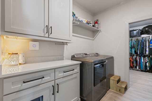 laundry room with washing machine and clothes dryer, light hardwood / wood-style floors, and cabinets