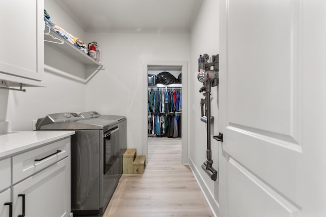 clothes washing area with cabinets, washing machine and dryer, crown molding, and light hardwood / wood-style floors