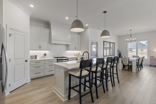 kitchen featuring gas stove, custom exhaust hood, decorative light fixtures, white cabinets, and a kitchen island with sink