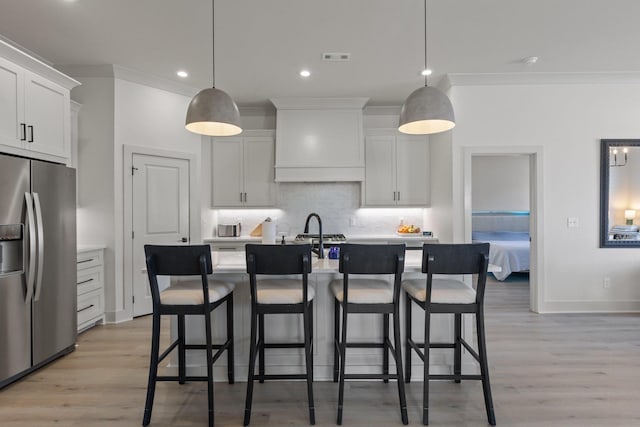 kitchen featuring decorative light fixtures, an island with sink, white cabinetry, and stainless steel fridge with ice dispenser