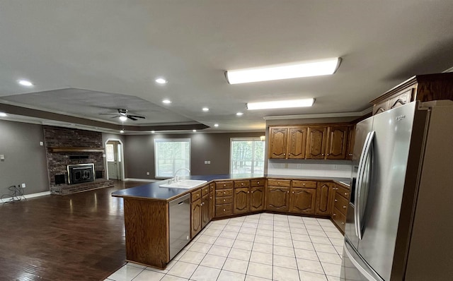 kitchen with kitchen peninsula, stainless steel appliances, sink, ornamental molding, and a raised ceiling