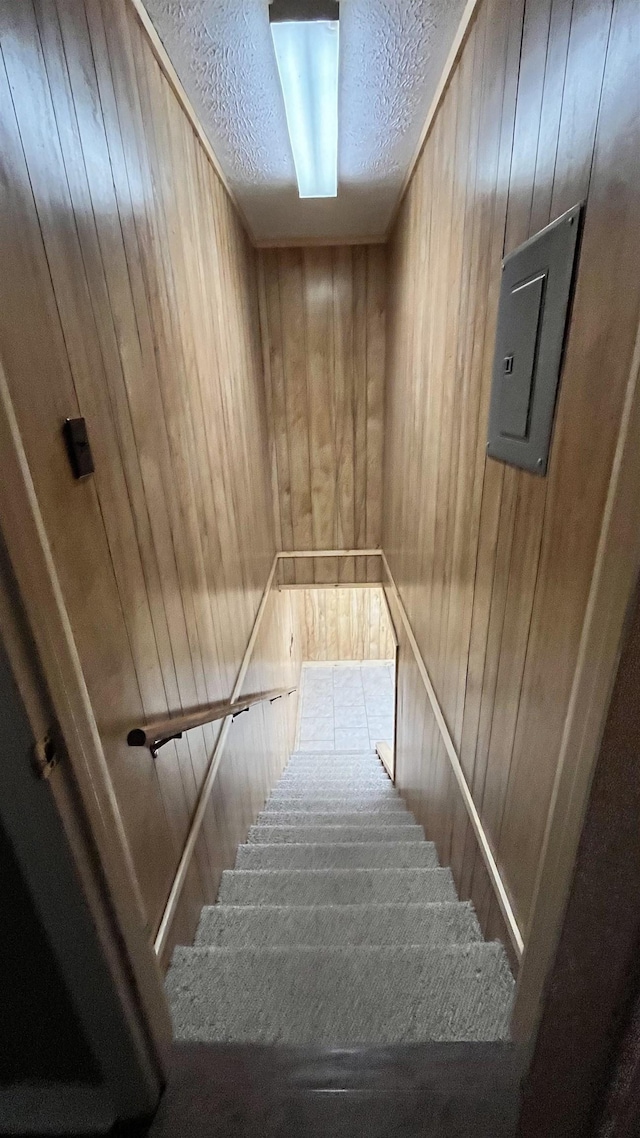 staircase with a textured ceiling and wooden walls