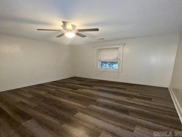 spare room with dark wood-type flooring, a ceiling fan, and baseboards