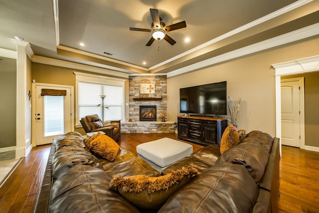 living room featuring a tray ceiling, hardwood / wood-style floors, crown molding, and a stone fireplace