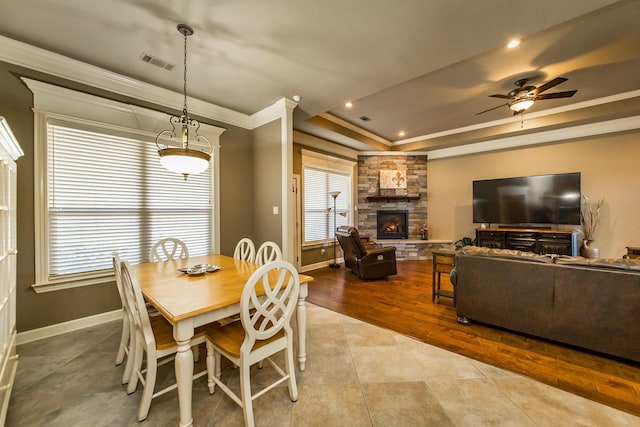 dining area featuring light tile patterned floors, ceiling fan, a raised ceiling, a fireplace, and ornamental molding