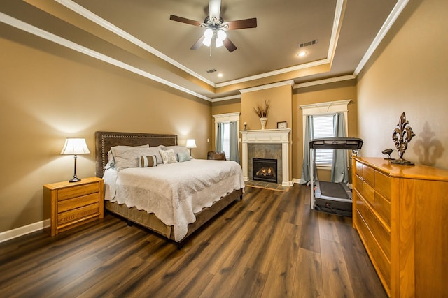 bedroom featuring a tray ceiling, ornamental molding, a tile fireplace, and dark hardwood / wood-style floors